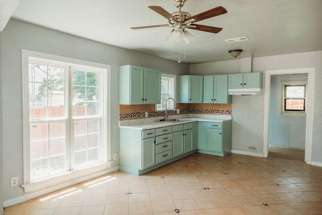 kitchen with a sink, green cabinets, ceiling fan, baseboards, and light countertops