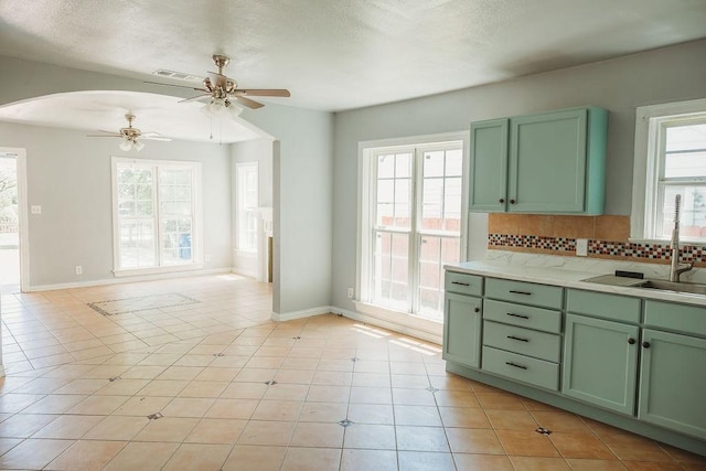 kitchen featuring green cabinetry, a sink, a ceiling fan, arched walkways, and tasteful backsplash