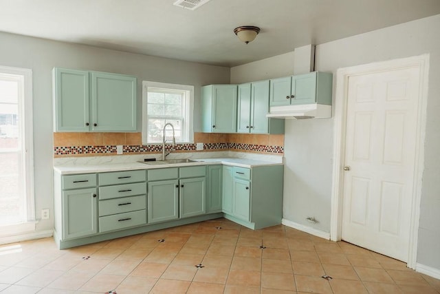 kitchen featuring a sink, green cabinets, backsplash, light countertops, and baseboards