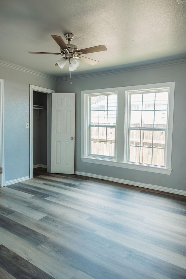 unfurnished bedroom featuring baseboards, crown molding, a closet, wood finished floors, and a textured ceiling