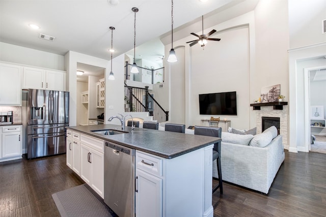 6108 Lipan Ln, Mckinney, TX 75070 - kitchen featuring appliances with stainless steel finishes, dark countertops, a sink, a stone fireplace, and dark wood-style flooring