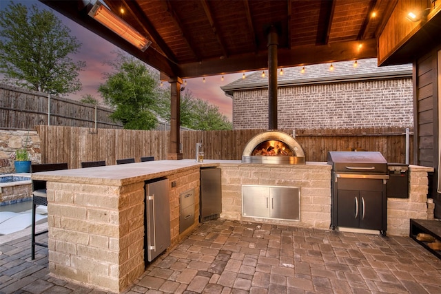 6108 Lipan Ln, Mckinney, TX 75070 - patio terrace at dusk featuring exterior kitchen, a fenced backyard, area for grilling, and exterior bar