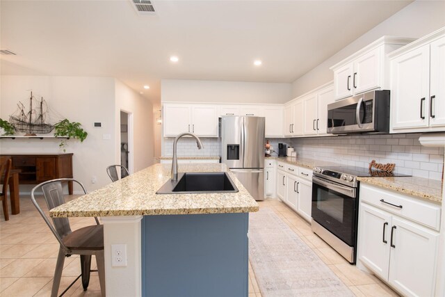 9332 Castorian Dr, Fort Worth, TX 76131 - kitchen featuring appliances with stainless steel finishes, a sink, backsplash, light tile patterned floors, and an island with sink
