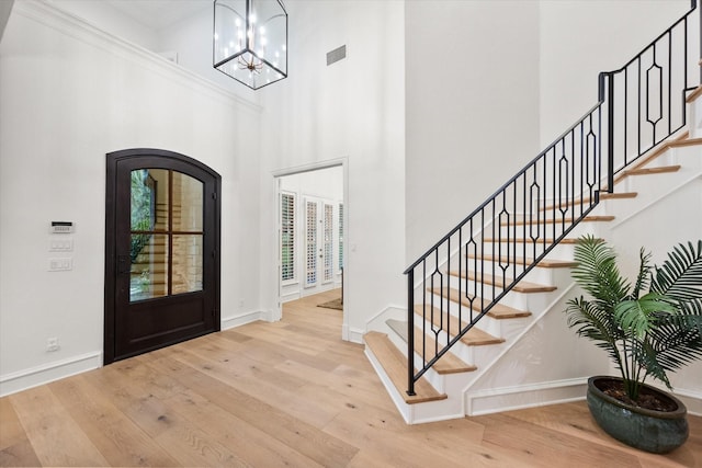 entryway with baseboards, wood finished floors, stairs, a chandelier, and a towering ceiling
