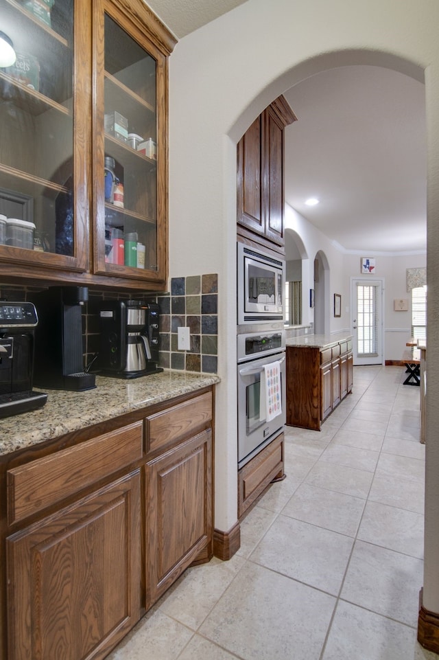 6001 Lacebark Elm Dr, Fort Worth, TX 76123 - kitchen with appliances with stainless steel finishes, light tile patterned flooring, arched walkways, backsplash, and glass insert cabinets