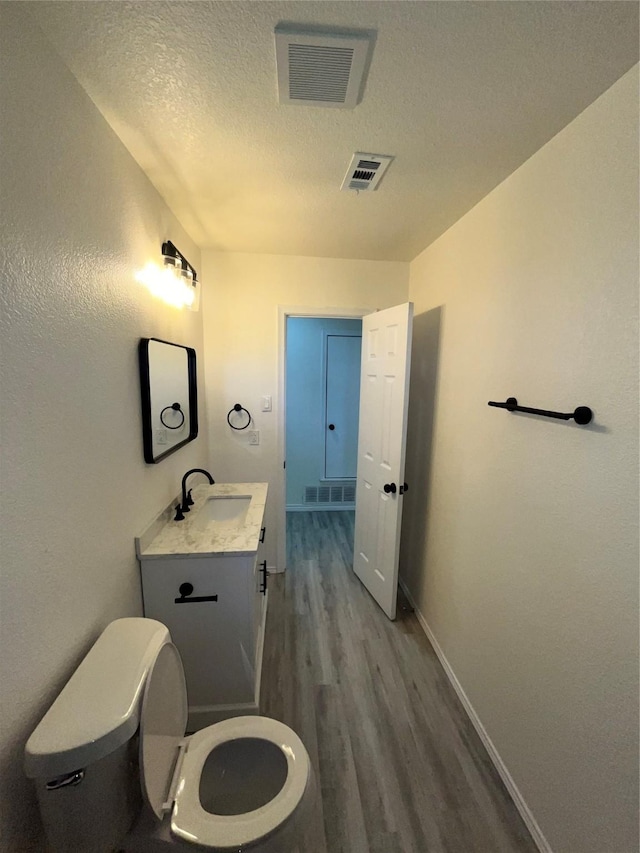6706 Frontage Rd, Greenville, TX 75402 - half bathroom featuring wood finished floors, a textured ceiling, toilet, vanity, and baseboards