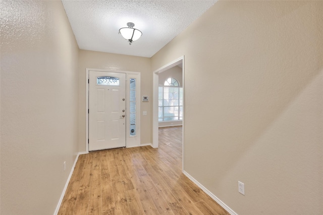 entryway featuring baseboards, light wood-style flooring, and a textured ceiling
