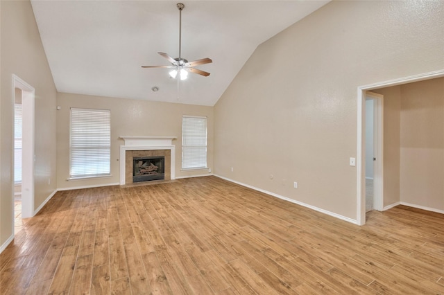 unfurnished living room with vaulted ceiling, a ceiling fan, light wood-type flooring, a tiled fireplace, and baseboards