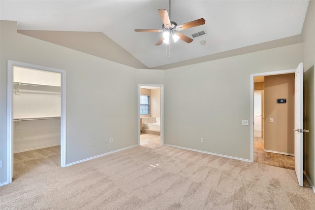 unfurnished bedroom with a spacious closet, lofted ceiling, carpet flooring, baseboards, and ensuite bath