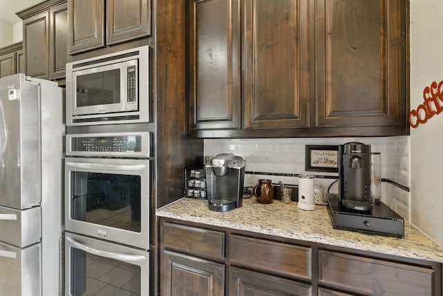 711 Red Stone Ln, Weatherford, TX 76087 - kitchen featuring appliances with stainless steel finishes, dark brown cabinetry, tasteful backsplash, light stone counters, and tile patterned flooring