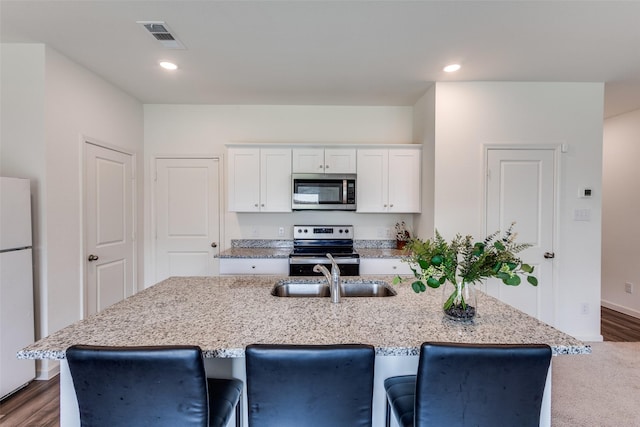 2115 Revere Dr, Princeton, TX 75407 - kitchen with stainless steel appliances, a sink, white cabinets, light stone counters, and a kitchen island with sink