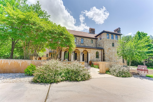 mediterranean / spanish house featuring stone siding, covered porch, a chimney, and fence