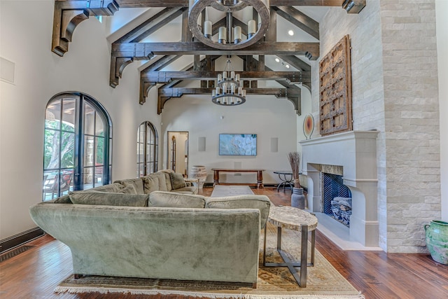 living area with a towering ceiling, a chandelier, wood finished floors, beam ceiling, and a fireplace