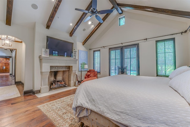 bedroom with beam ceiling, wood finished floors, multiple windows, a high end fireplace, and arched walkways