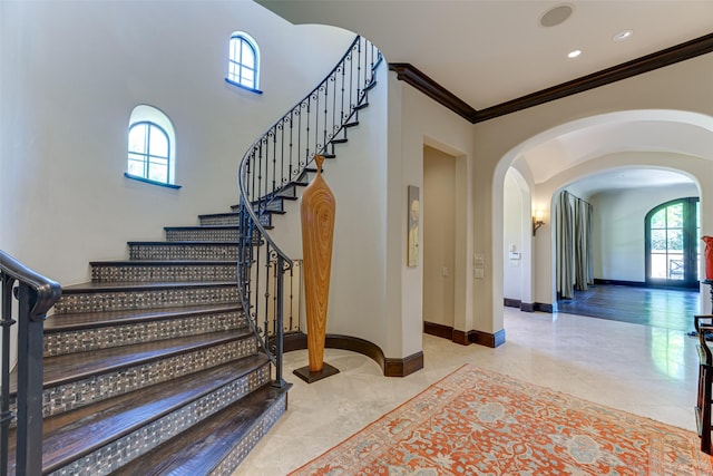 stairs with arched walkways, ornamental molding, tile patterned flooring, and baseboards