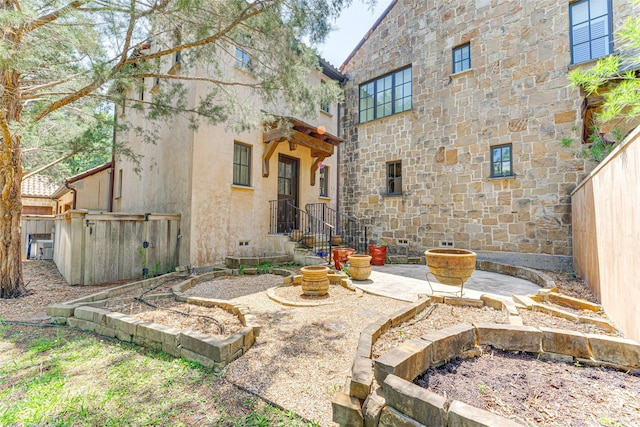 back of property featuring stone siding, fence, and stucco siding