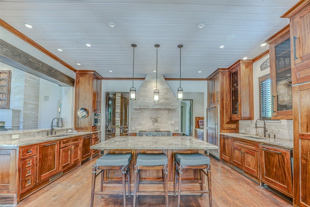 kitchen with a sink, light stone counters, wall chimney exhaust hood, ornamental molding, and light wood-type flooring