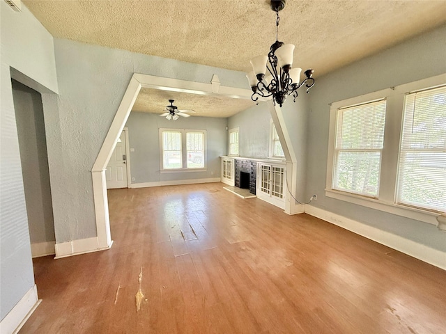 unfurnished living room with a textured ceiling, wood finished floors, baseboards, a fireplace with raised hearth, and ceiling fan