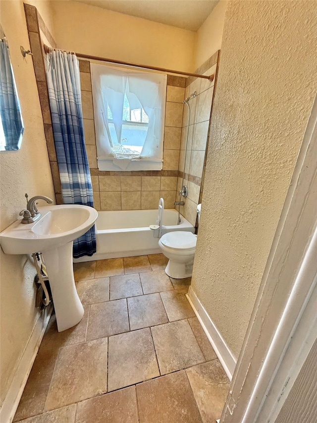 full bath with a textured wall, shower / bathtub combination with curtain, toilet, and baseboards