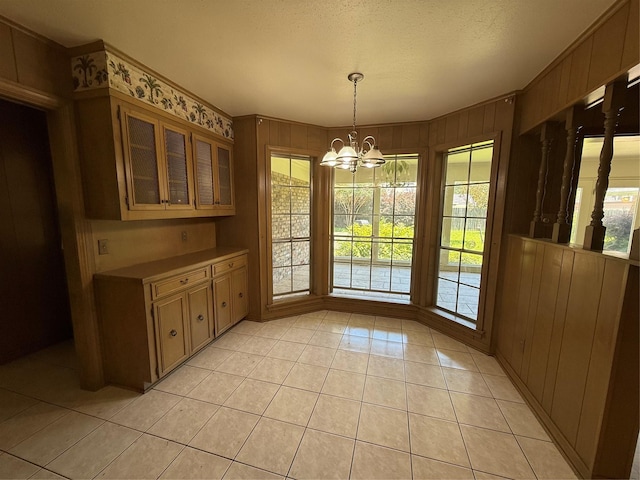 8309 Ashbourne Dr, Shreveport, LA 71106 - unfurnished dining area with light tile patterned flooring, a chandelier, plenty of natural light, wood walls, and a textured ceiling