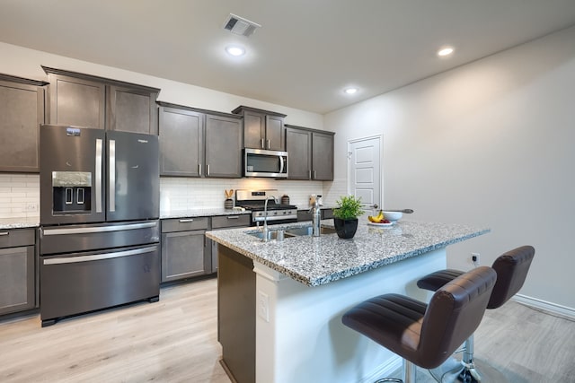 2825 Hale Rd, Celina, TX 75009 - kitchen featuring appliances with stainless steel finishes, light stone countertops, a breakfast bar, light wood-style flooring, and backsplash
