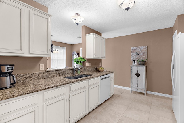 kitchen featuring dishwashing machine, freestanding refrigerator, a sink, dark stone countertops, and baseboards