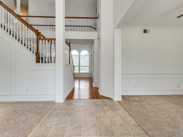 entryway with a decorative wall, stairs, light carpet, ceiling fan, and ornamental molding