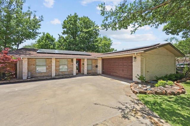 view of front of property with driveway, an attached garage, solar panels, and brick siding