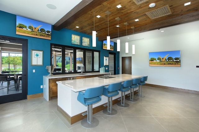 bar with baseboards, light tile patterned floors, a sink, beamed ceiling, and decorative light fixtures