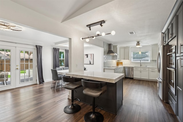 10834 Wyatt St, Dallas, TX 75218 - kitchen with wall chimney range hood, appliances with stainless steel finishes, backsplash, a sink, and a center island