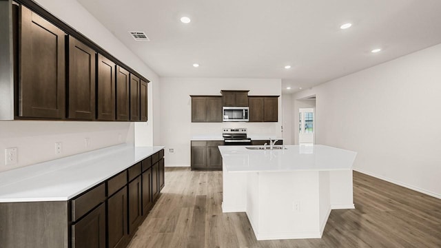 440 Drake Dr, Ferris, TX 75125 - kitchen featuring appliances with stainless steel finishes, light wood-type flooring, dark brown cabinetry, light countertops, and an island with sink