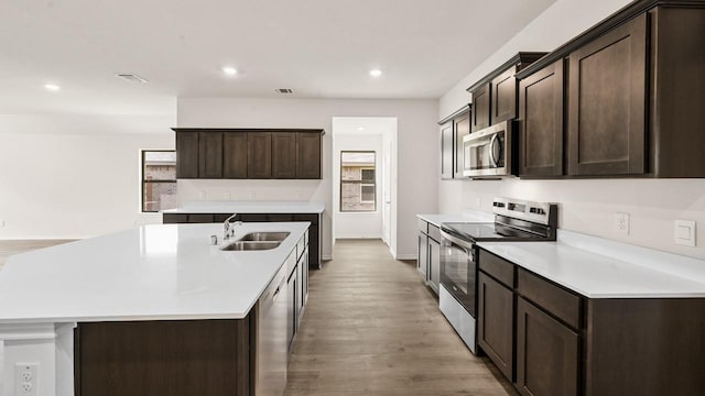 440 Drake Dr, Ferris, TX 75125 - kitchen featuring stainless steel appliances, a kitchen island with sink, dark brown cabinetry, light wood-style flooring, and recessed lighting