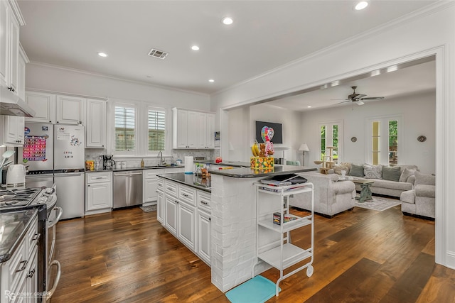 kitchen with appliances with stainless steel finishes, dark countertops, white cabinets, ceiling fan, and ornamental molding