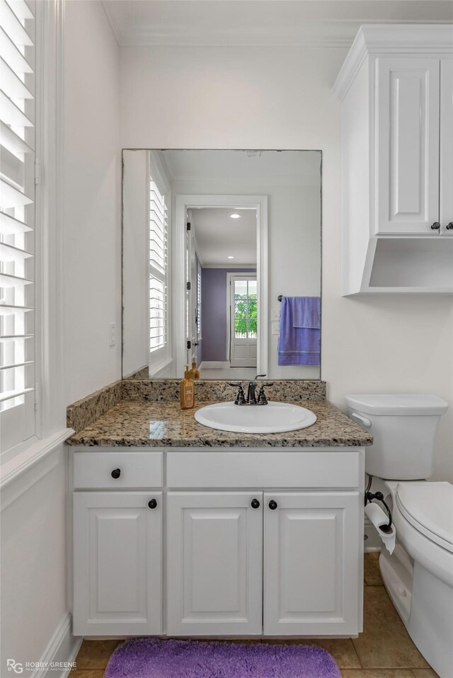 half bathroom featuring toilet, vanity, tile patterned floors, ornamental molding, and baseboards