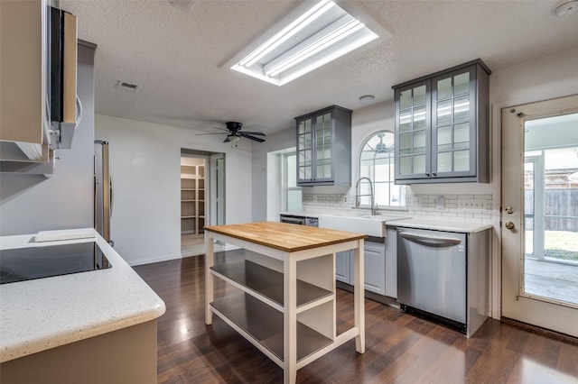 kitchen with stainless steel dishwasher, wood counters, a sink, decorative backsplash, and a textured ceiling