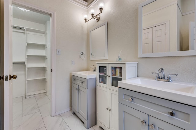 bathroom featuring marble look tile flooring, two vanities, a spacious closet, and baseboards
