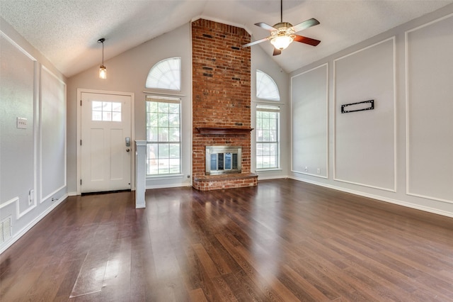 unfurnished living room featuring a decorative wall, dark wood-style flooring, a ceiling fan, a brick fireplace, and high vaulted ceiling