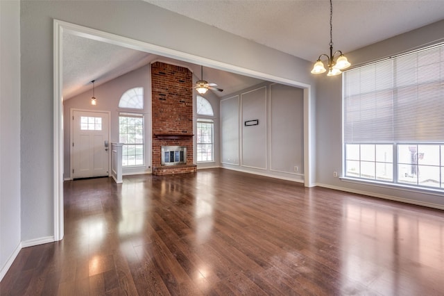 unfurnished living room featuring a fireplace, a chandelier, vaulted ceiling, dark wood-style floors, and baseboards