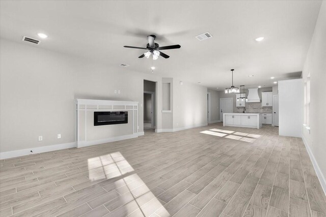 4405 Baylor St, Fort Worth, TX 76119 - unfurnished living room featuring light wood-style floors, a ceiling fan, baseboards, a chandelier, and a glass covered fireplace