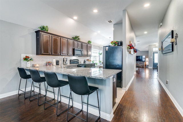 4002 Silver Lake Trl, Heartland, TX 75126 - kitchen featuring stainless steel appliances, a peninsula, dark brown cabinets, dark wood-style floors, and a breakfast bar area