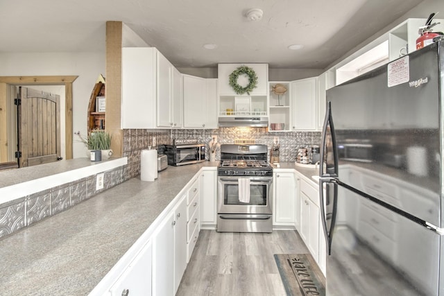 179 Oak St, Nocona, TX 76255 - kitchen with appliances with stainless steel finishes, under cabinet range hood, open shelves, white cabinetry, and decorative backsplash