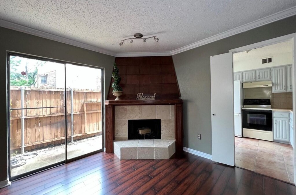883 Dublin Dr Unit 1, Richardson, TX 75080 - unfurnished living room with wood finished floors, a tiled fireplace, a textured ceiling, ornamental molding, and baseboards
