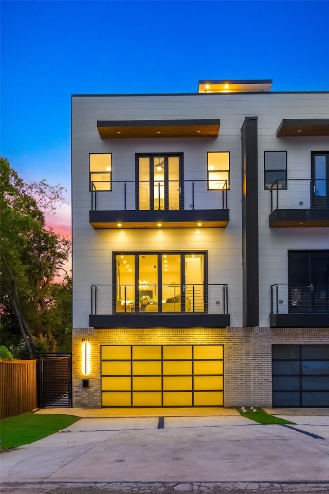 1921 Pollard St, Dallas, TX 75208 - back of property at dusk featuring a balcony, fence, a garage, brick siding, and driveway