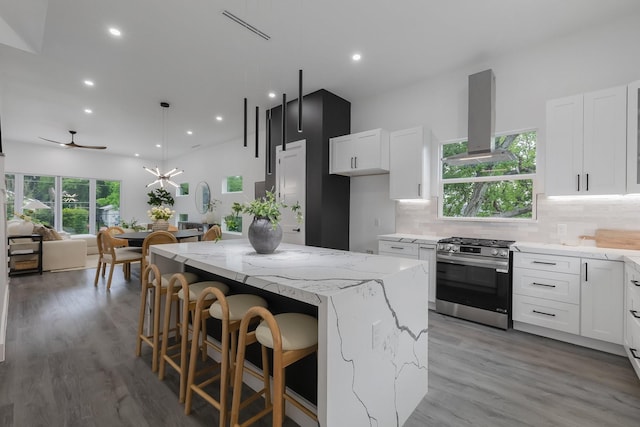 1921 Pollard St, Dallas, TX 75208 - kitchen with gas range, wall chimney exhaust hood, light stone counters, a kitchen island, and decorative backsplash