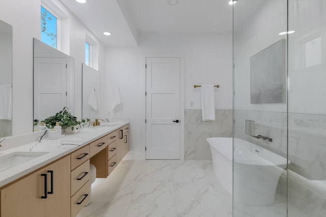 1921 Pollard St, Dallas, TX 75208 - bathroom featuring a soaking tub, marble finish floors, double vanity, recessed lighting, and a wainscoted wall