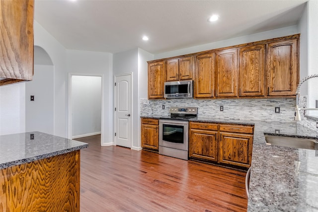 2007 Brazoria Dr, Forney, TX 75126 - kitchen featuring stainless steel appliances, a sink, dark stone counters, decorative backsplash, and wood finished floors
