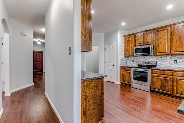 2007 Brazoria Dr, Forney, TX 75126 - kitchen featuring stainless steel appliances, wood finished floors, dark stone counters, arched walkways, and tasteful backsplash