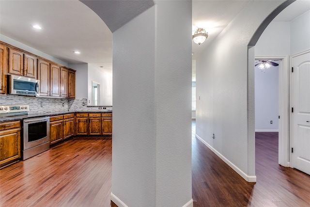 2007 Brazoria Dr, Forney, TX 75126 - kitchen with appliances with stainless steel finishes, arched walkways, dark wood finished floors, brown cabinetry, and decorative backsplash