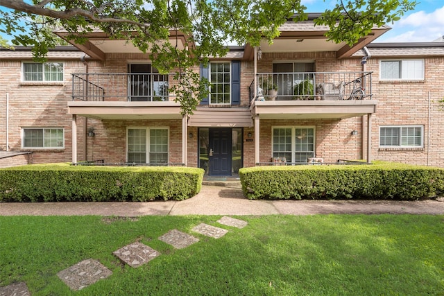 multi unit property with a balcony, a front yard, and brick siding