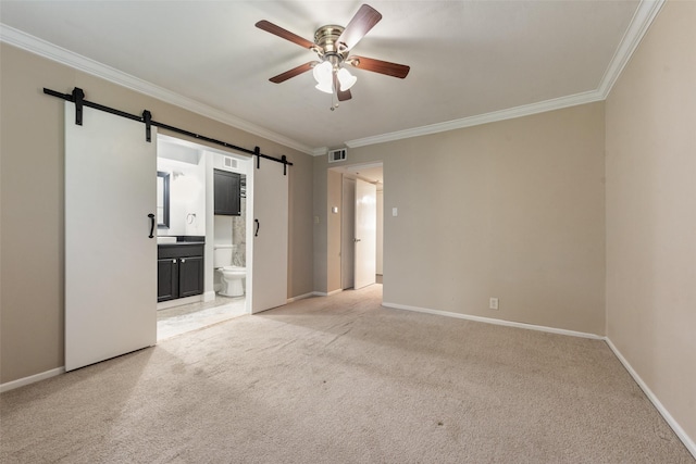 empty room featuring a barn door, crown molding, ceiling fan, light colored carpet, and baseboards